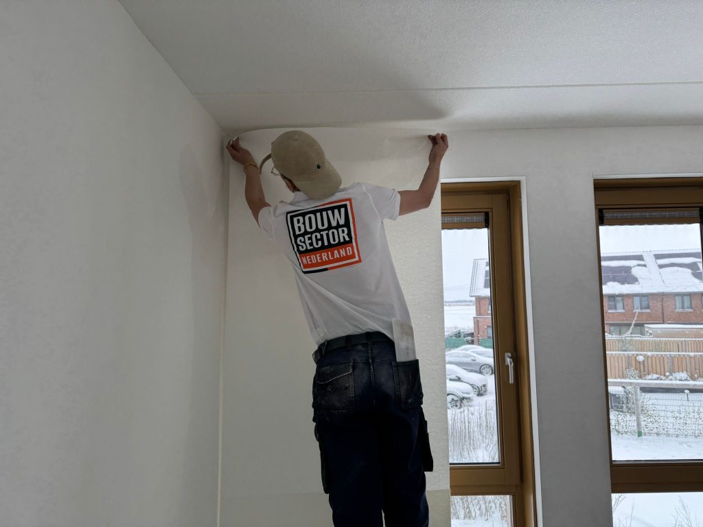 Vakman van Bouwsector Nederland zet een baan behang vast tot tegen het plafond