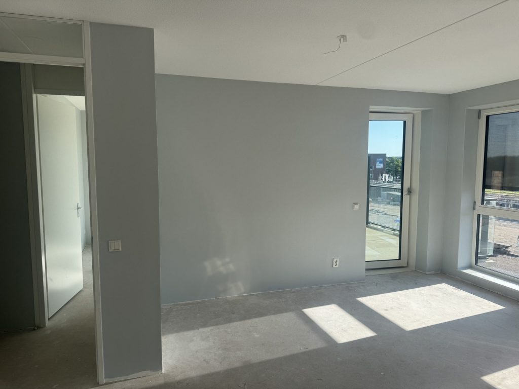Kamer met lichtgrijs gesausde wanden, een balkondeur en zon op de betonvloer