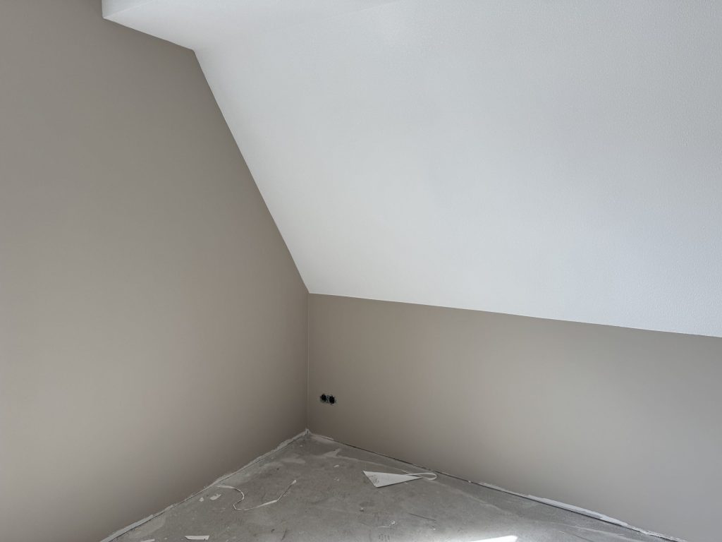 Zolderkamer met een schuine wand, strak gesausd in een lichte taupe tint