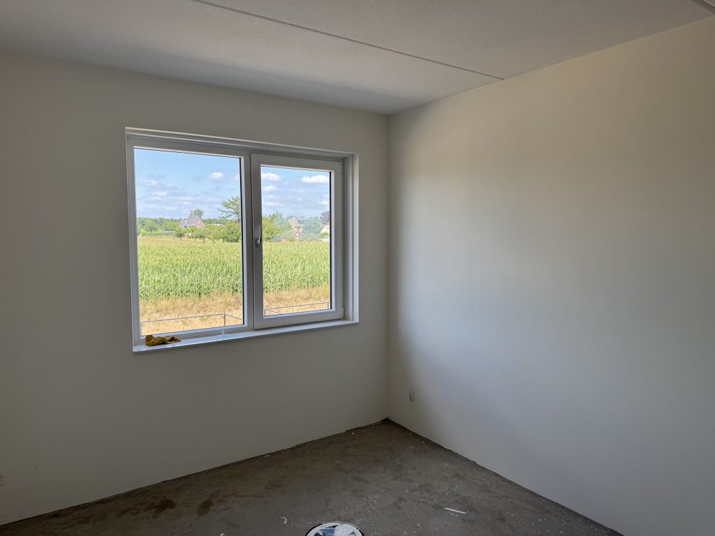 Lege nieuwbouwkamer met gladde lichte wanden en een raam met uitzicht op een maisveld
